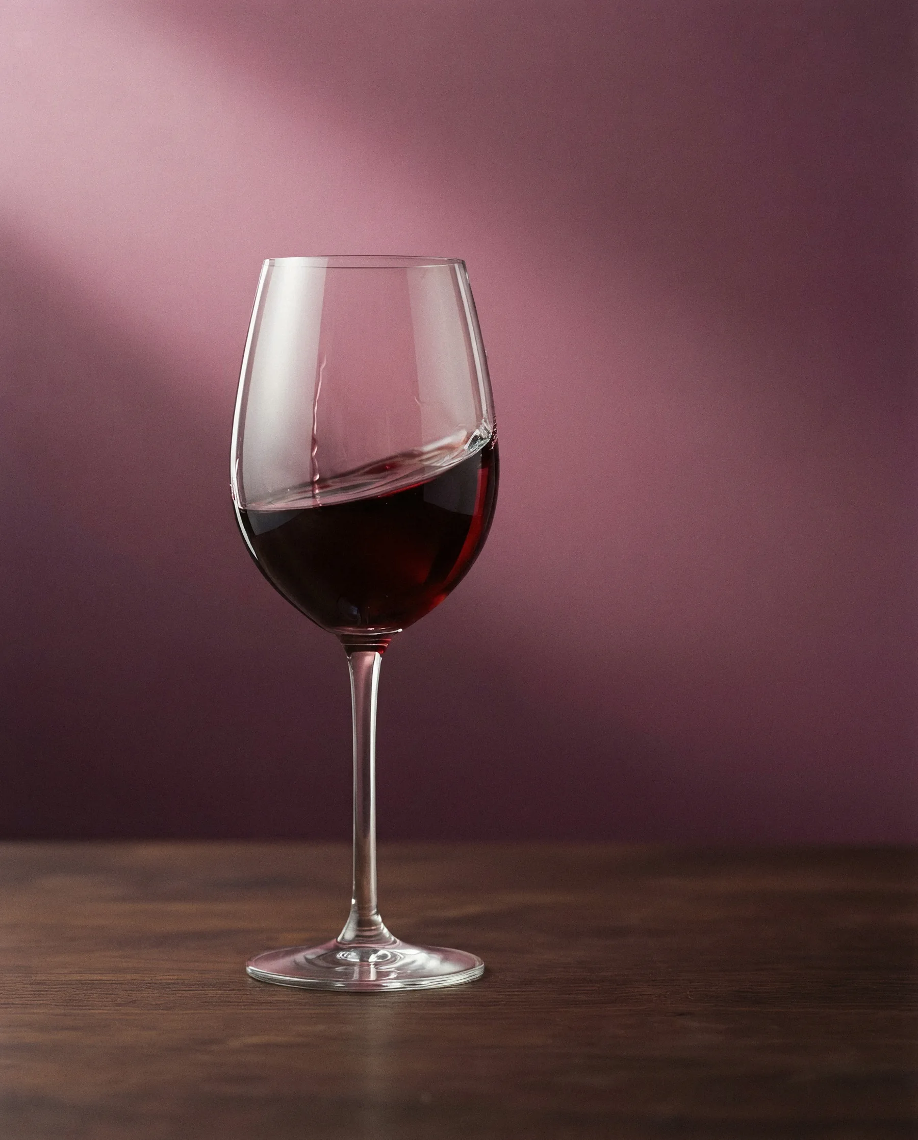 Calice di vino rosso in movimento su fondale malva, colpito da un fascio di luce
